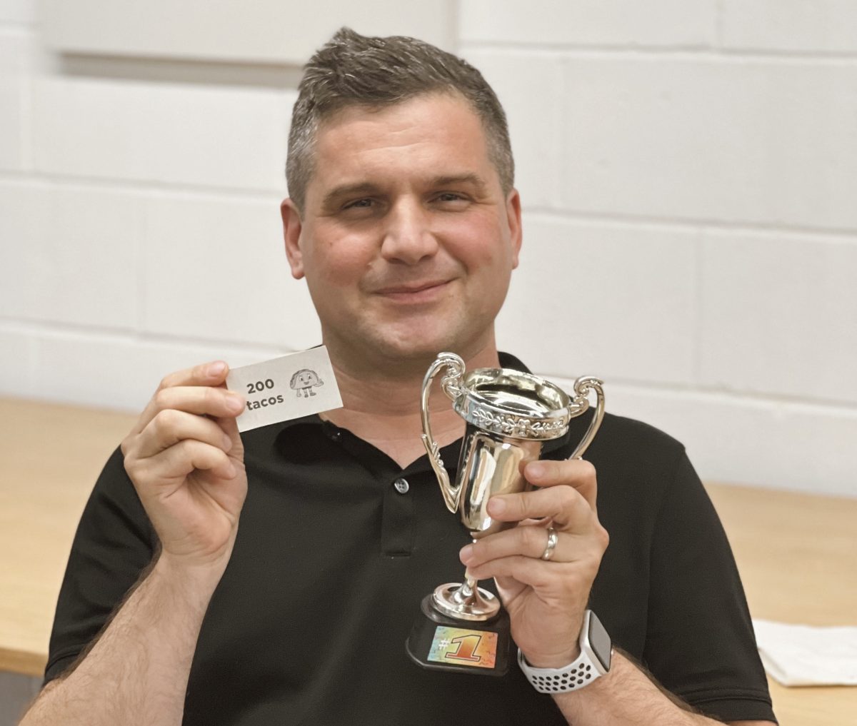 Man smiling holding a trophy and a reward ticket.